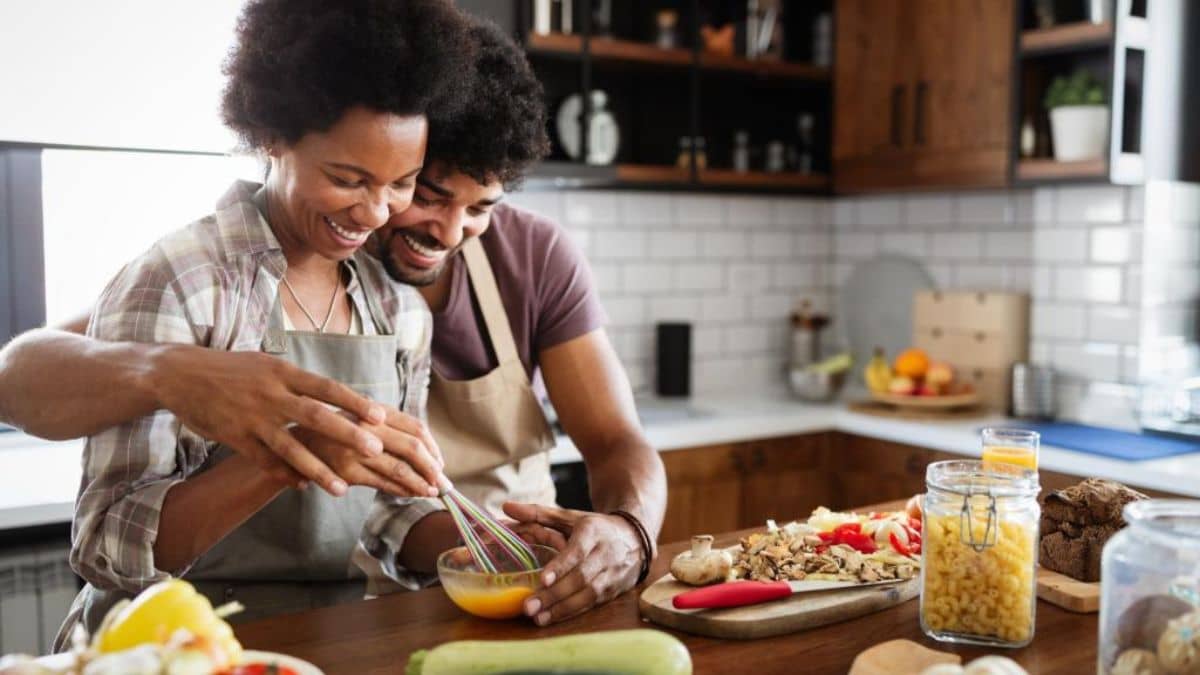 A couple cooking together in a kitchen, smiling as they whisk ingredients in a bowl.