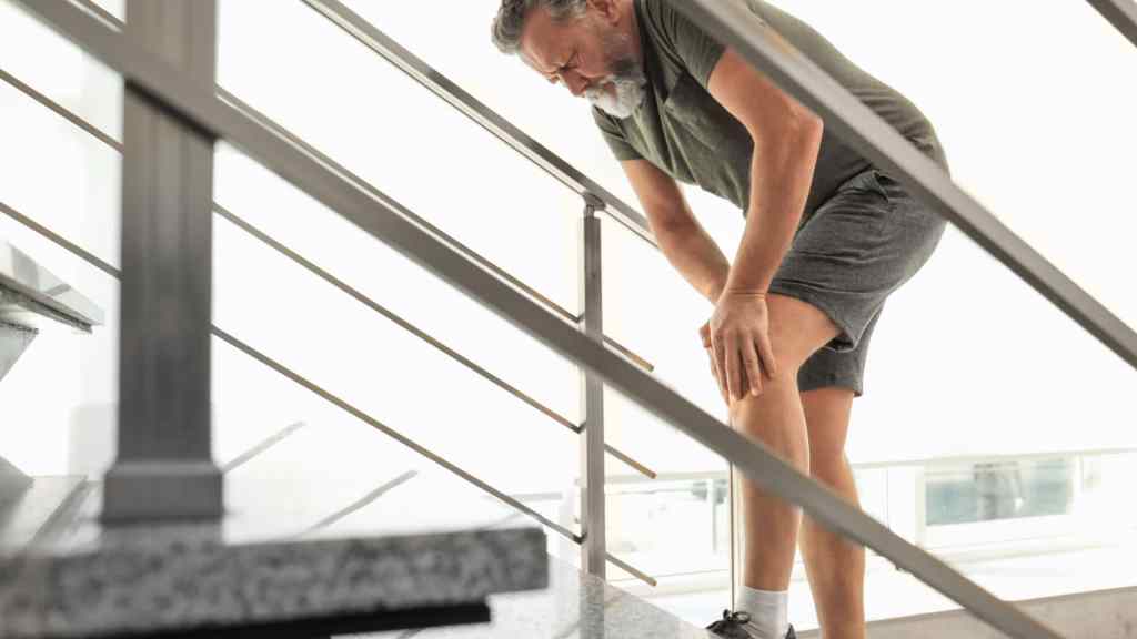 Man in athletic wear holding his knee while climbing stairs, looking pained.