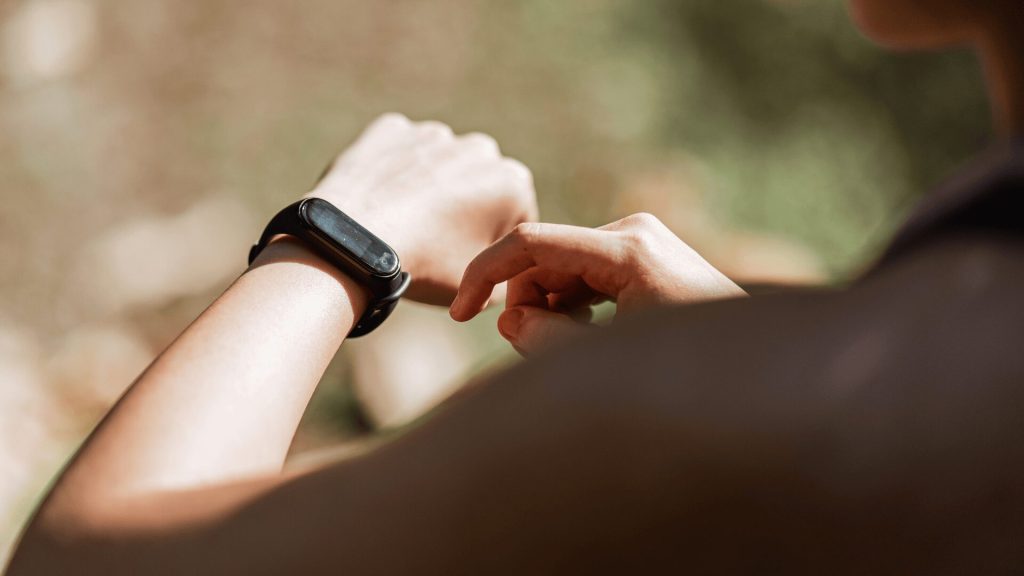 Person checking the screen of a fitness tracker or smartwatch on their wrist outdoors.