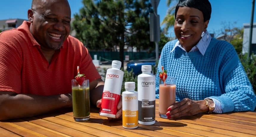 Two people sit at an outdoor table with four bottles of dietary supplements and two glasses of juice. They appear to be smiling and engaged in conversation.