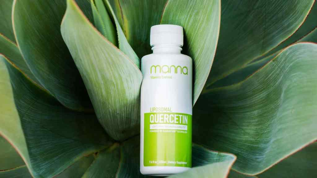 A bottle of Manna Liposomal Quercetin dietary supplement rests on large green plant leaves.