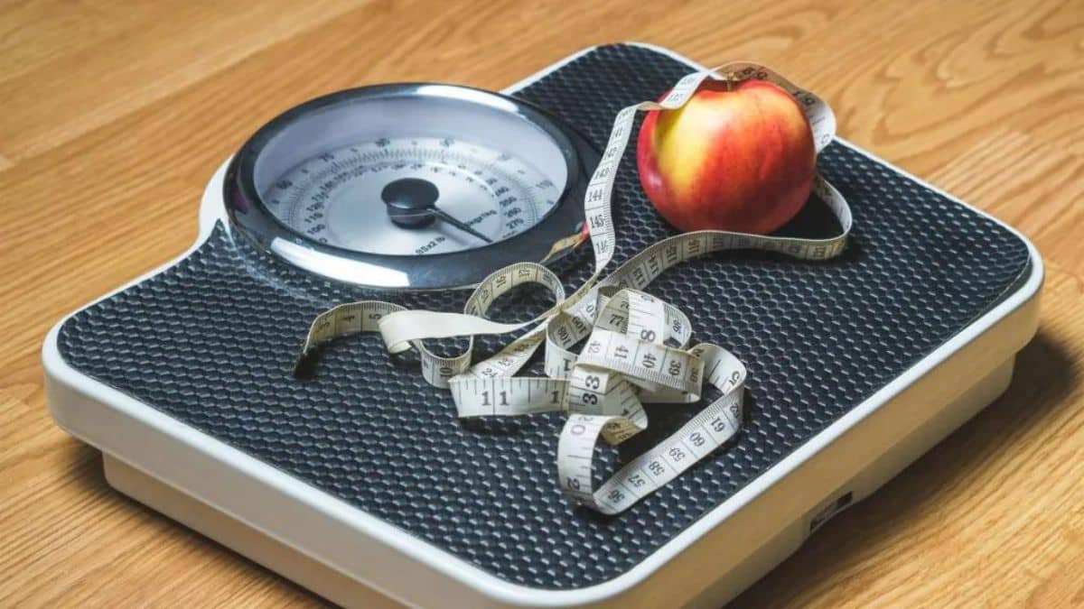 A bathroom scale with a measuring tape and an apple on it, symbolizing weight management and healthy eating.