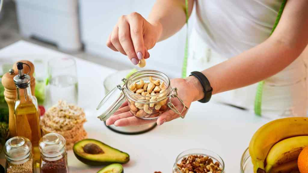 Person holding a jar of cashews over a table with avocados, bananas, and various foods.