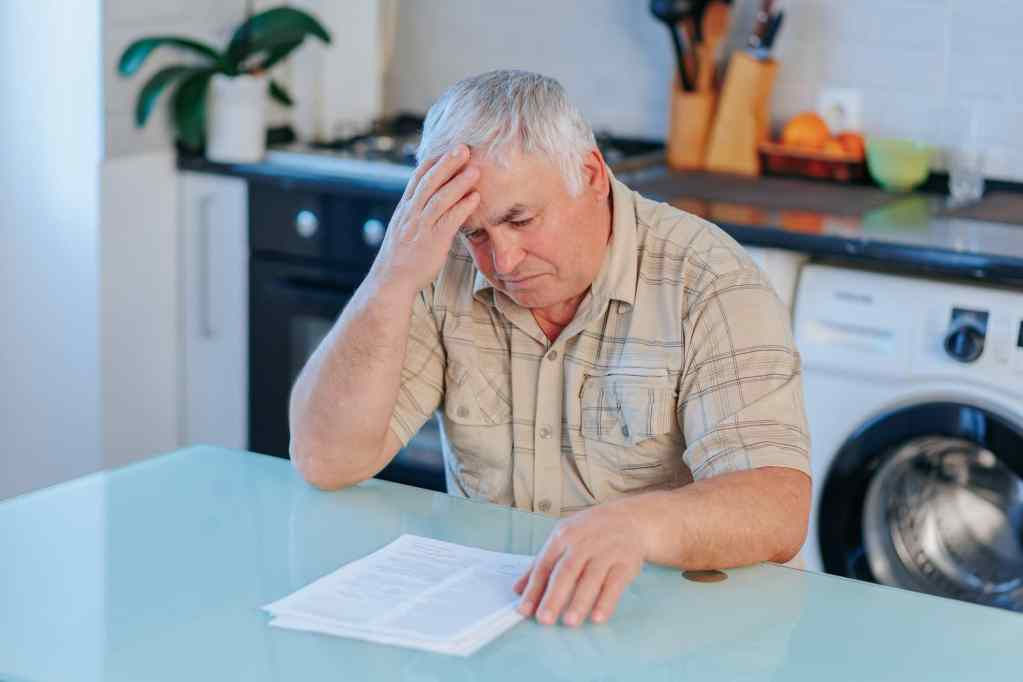 Elderly person looking at paper holding head