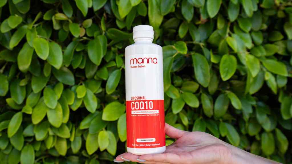 A hand holds a bottle of "mama Liposomal CoQ10" dietary supplement with a leafy green background.