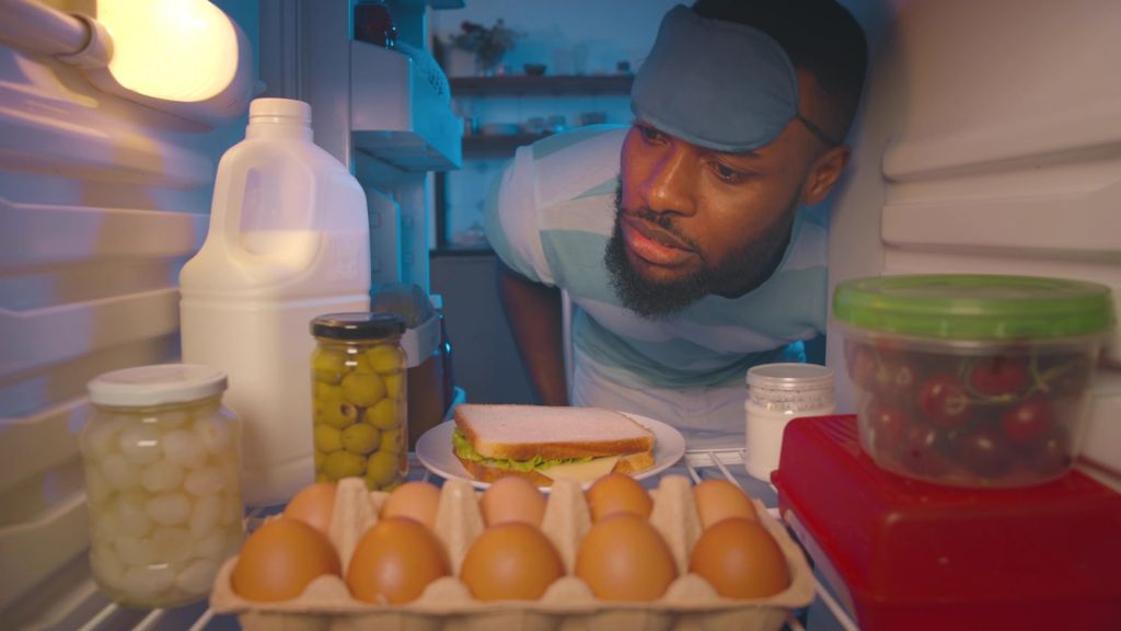 man with an eye mask on his forehead looking in the fridge for a snack