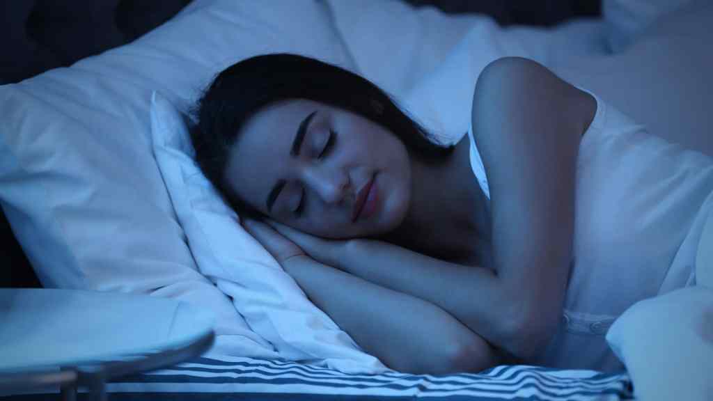 A person sleeping peacefully on a bed with white sheets, illuminated by a soft blue light.