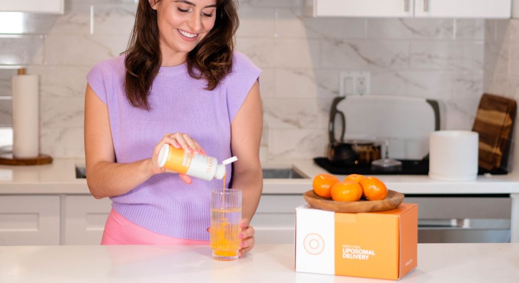 Woman pouring a supplement into a glass in a modern kitchen.