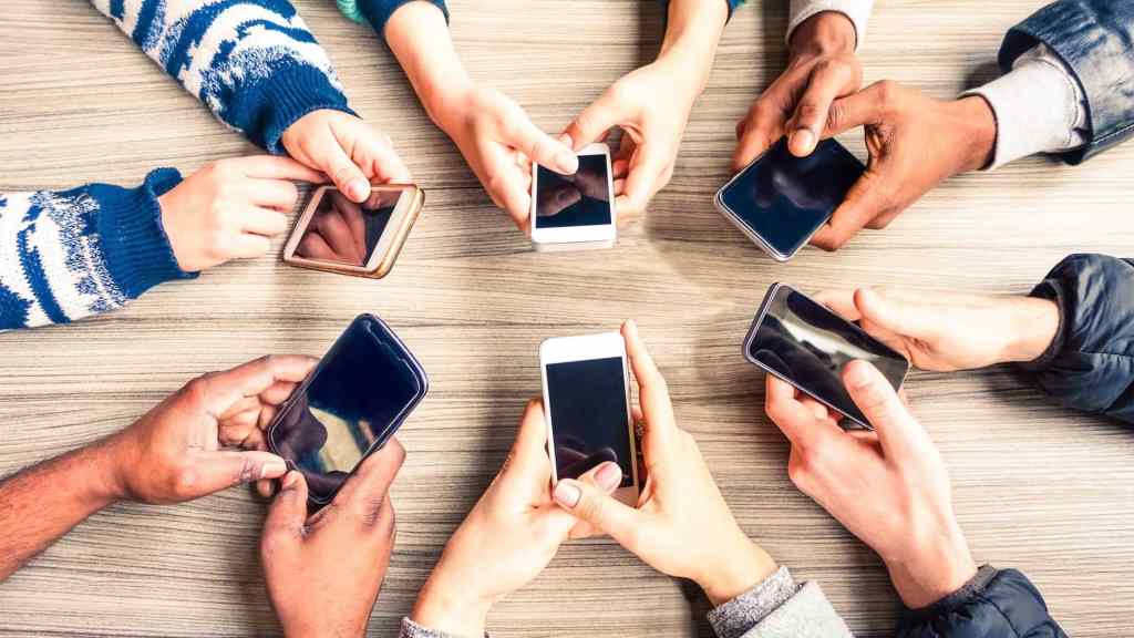A group of people sitting around a table, each holding a smartphone.