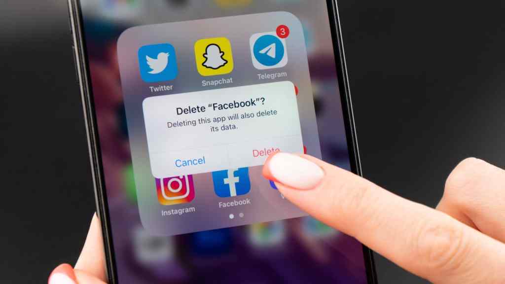 Close-up of a smartphone screen displaying a prompt asking to delete the Facebook app. A finger hovers over the delete option.
