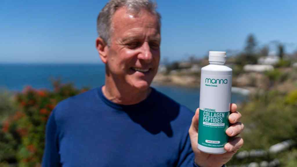 A man in a blue shirt holds a bottle of liposomal collagen peptides outdoors by the sea with greenery and buildings in the background.