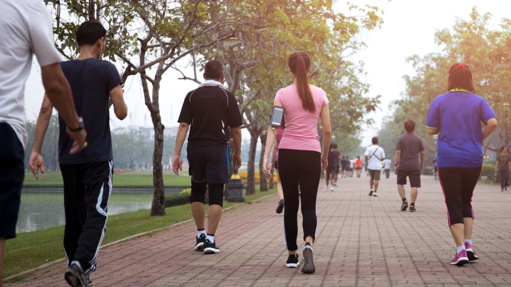 People walking on a paved path in a park, surrounded by trees, with some wearing casual and sports attire.