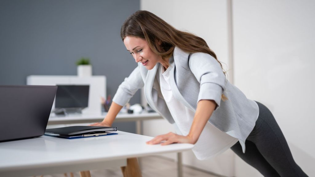 Professional woman doing a pushup against a desk