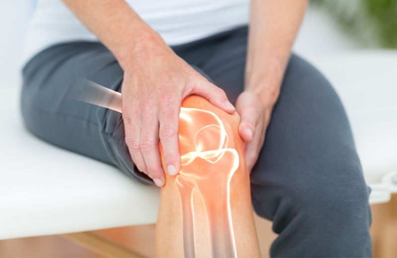 Person holding their knee in pain with an overlaid graphic of the knee joint