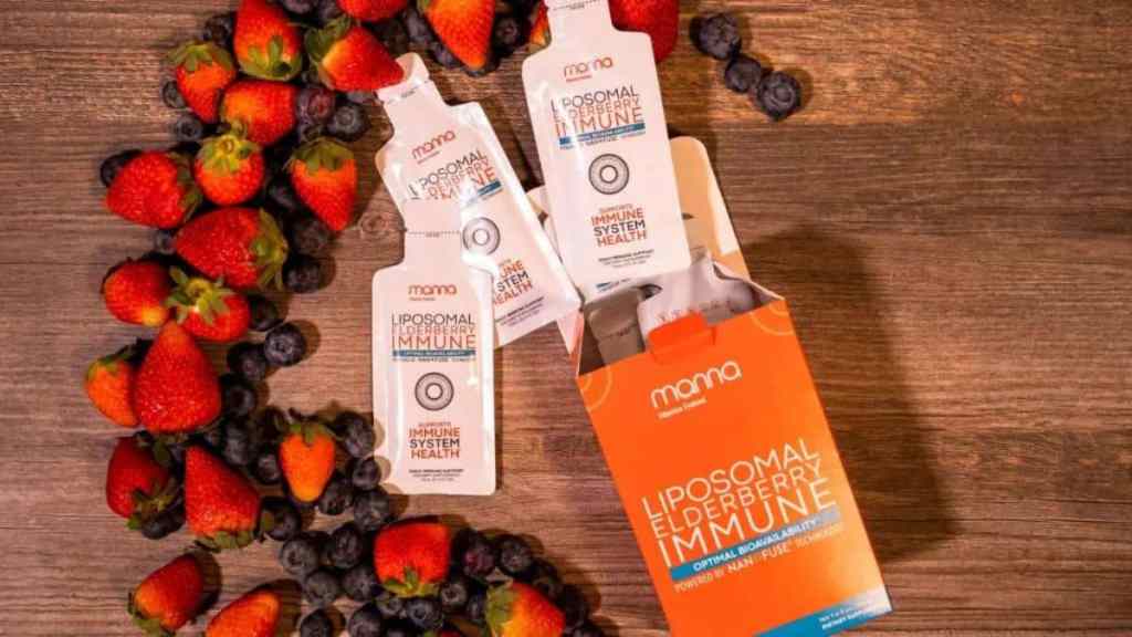 Box of Liposomal Elderberry Immune supplement surrounded by fresh strawberries and blueberries on a wooden surface.
