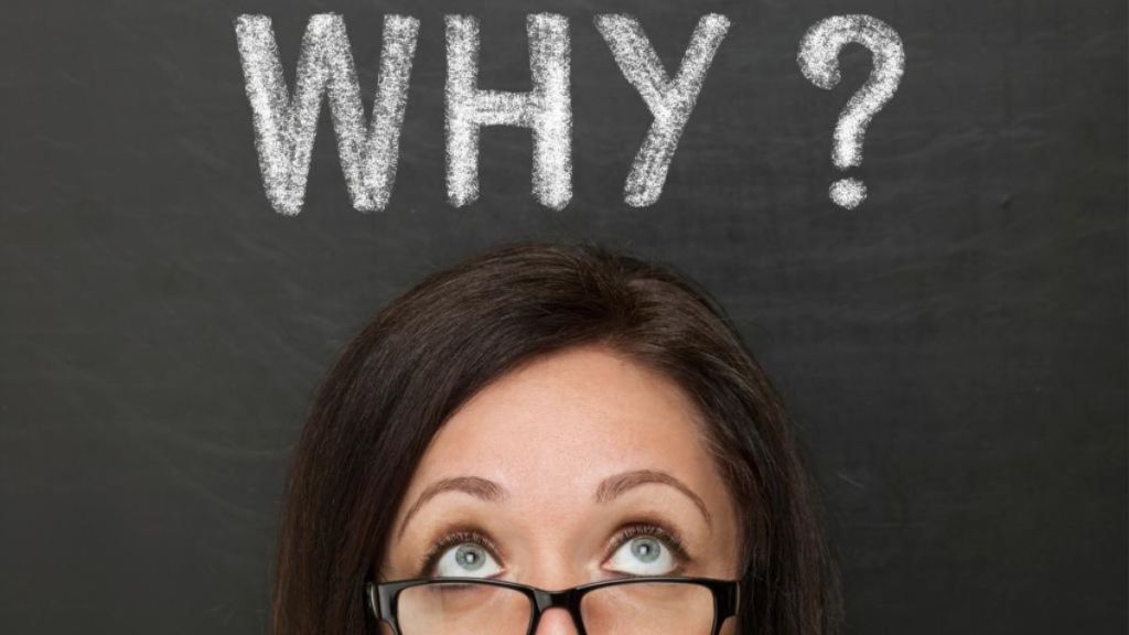 Woman with glasses looking up at the word "why?" written in chalk on a blackboard.