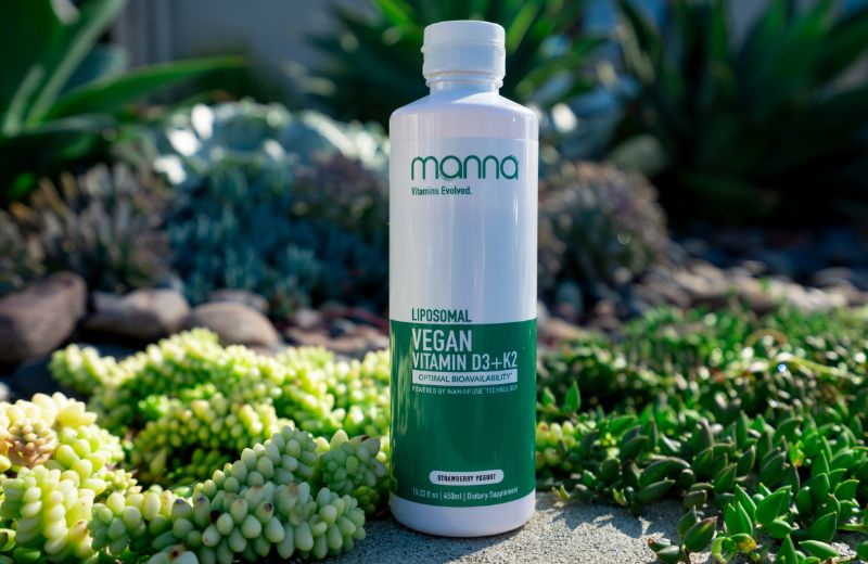 A bottle of Manna Vegan Vitamin D3-K2 surrounded by lush succulent plants, highlighted in natural sunlight.