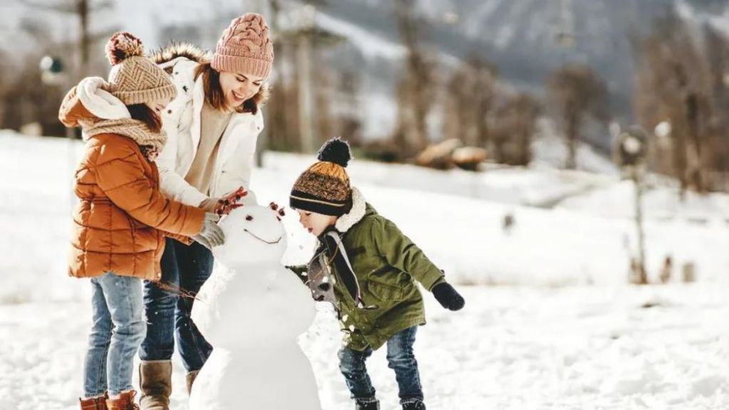 Family enjoys building a snowman together in a snowy landscape.