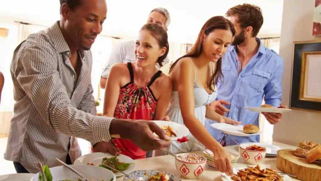 People serving themselves food at a casual buffet-style gathering.