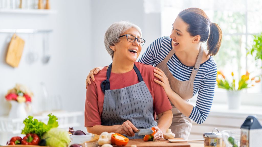 A younger and older woman in the kitchen smiling laughing