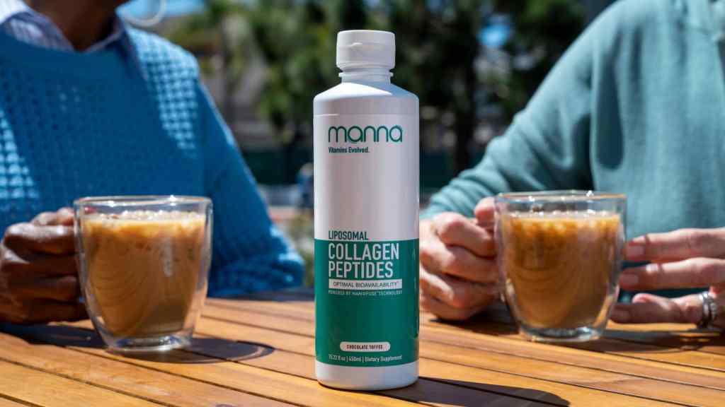A bottle of liposomal collagen peptides supplement sits on a wooden table between two people holding glasses of iced coffee.