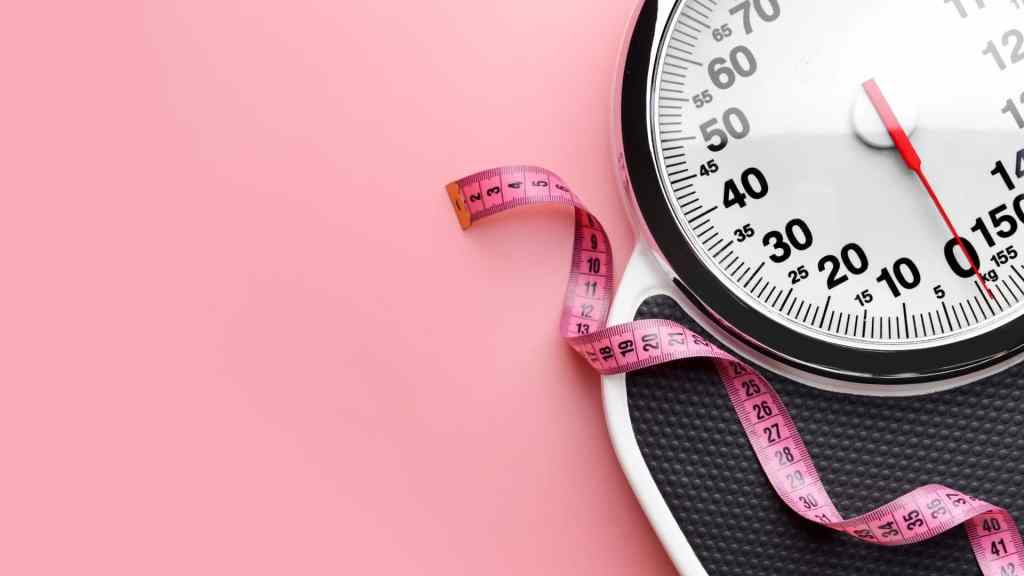 A bathroom scale with a pink measuring tape on a pink background.