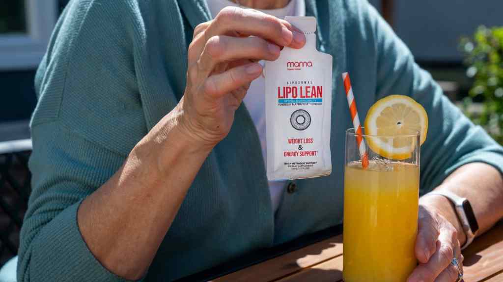 A person holding a Lipo Lean supplement sachet over a glass of orange juice with a straw and lemon slice.