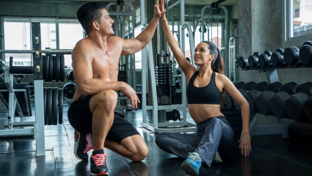 Fit man and woman seated in a gym high-fiving.