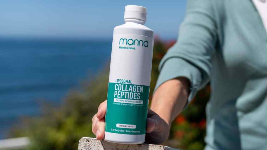 Person holding a bottle of Mama Liposomal Collagen Peptides supplement with a scenic ocean background.