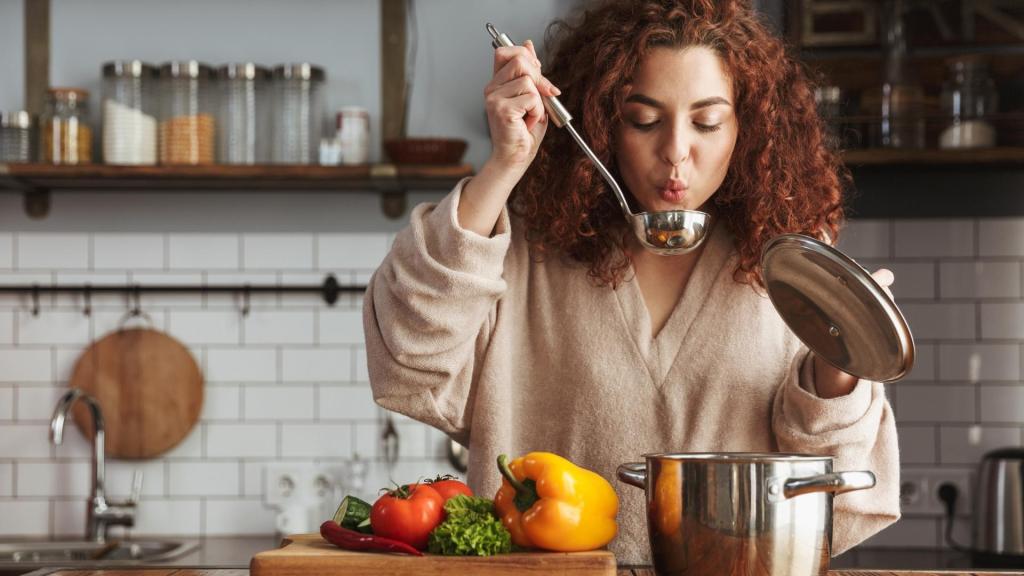 Woman cooking in the kitchen, blowing on a ladle of soup to cool it.