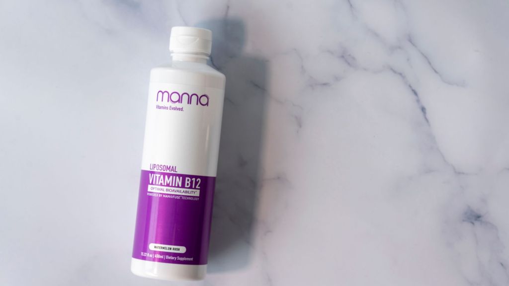 A bottle of Manna Liposomal Vitamin B12 stands against a marble background. The label is predominantly white and purple, featuring product information and branding.