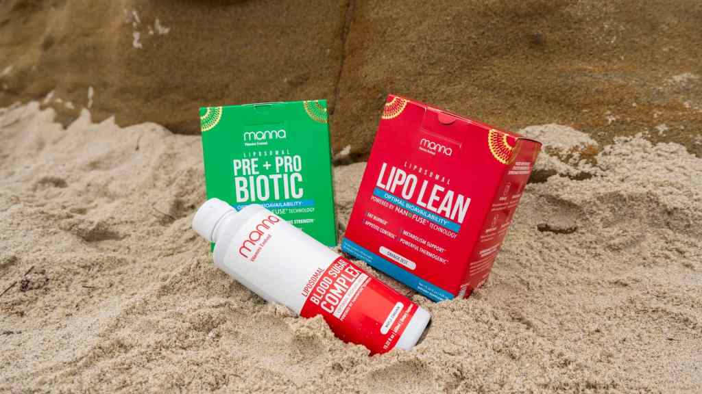 Three MOMA supplement products, including a bottle and two boxes labeled "PRE + PROBIOTIC" and "LIPOLEAN," are partially buried in sand with rocks in the background.
