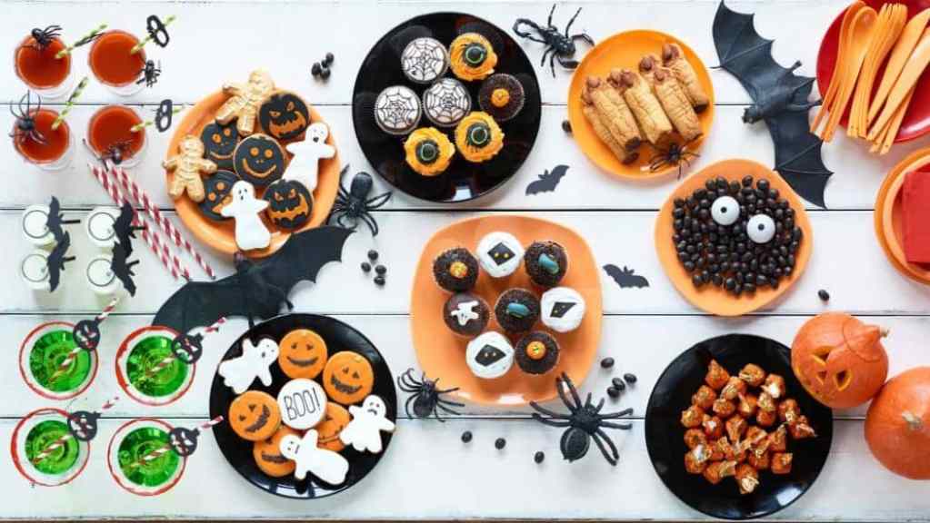 A festive halloween-themed table setting with decorative cookies, candies, and drinks.