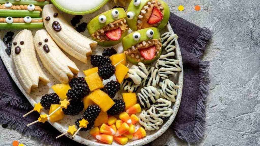 A creative and colorful arrangement of fruit and snacks fashioned into fun shapes and characters on a plate, intended to appeal to children.