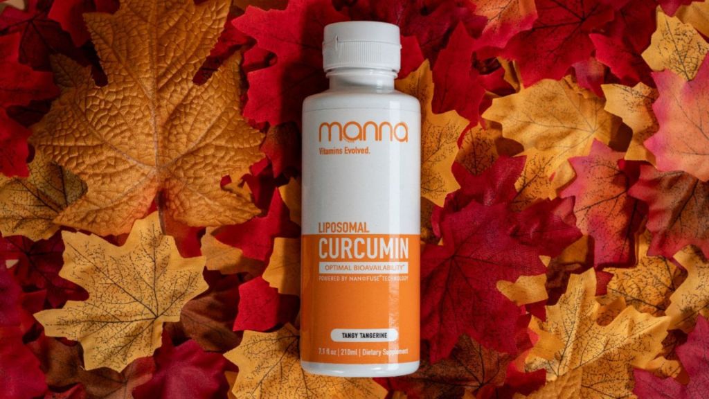 A bottle of Manna Liposomal Curcumin dietary supplement lies on a bed of autumn leaves.