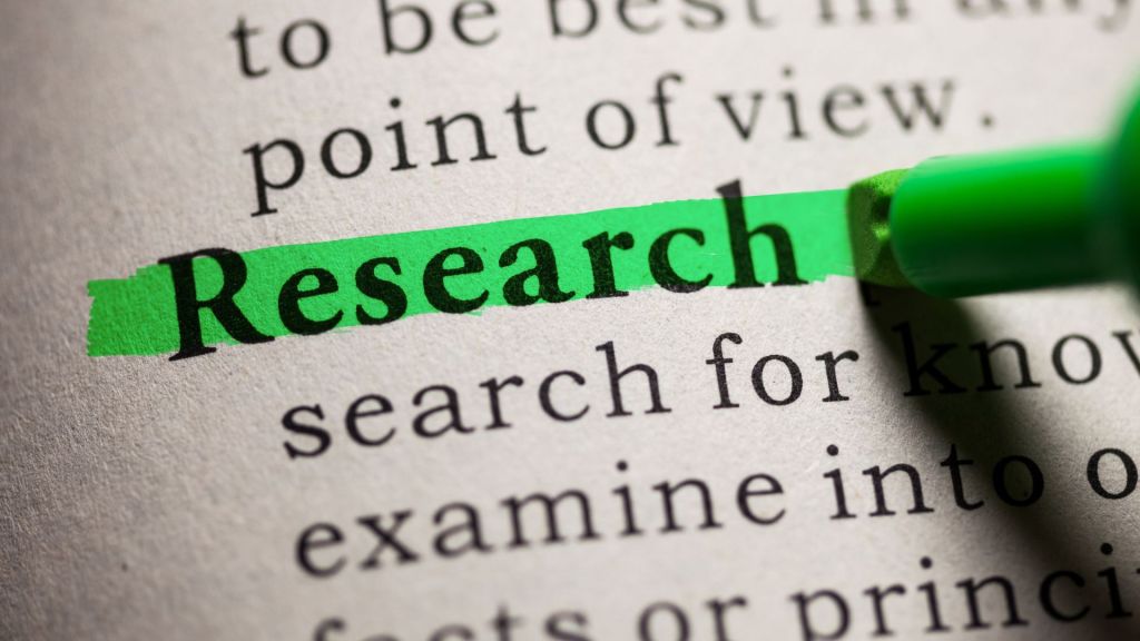 A close-up of the word "Research" being highlighted in green in a printed document.