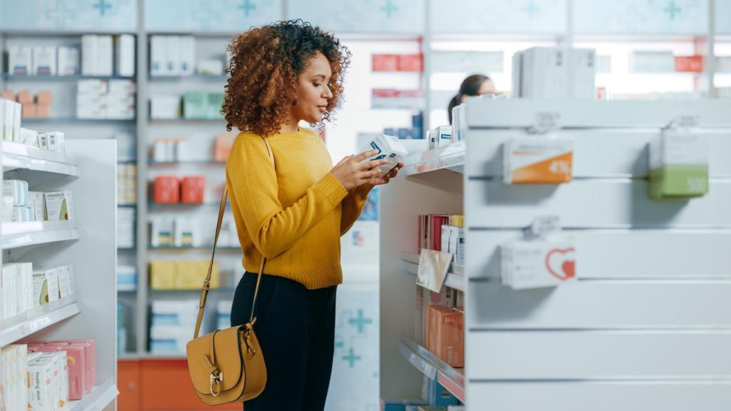 Woman shopping in a pharmacy aisle, reading the back of a boxed product in her hands.