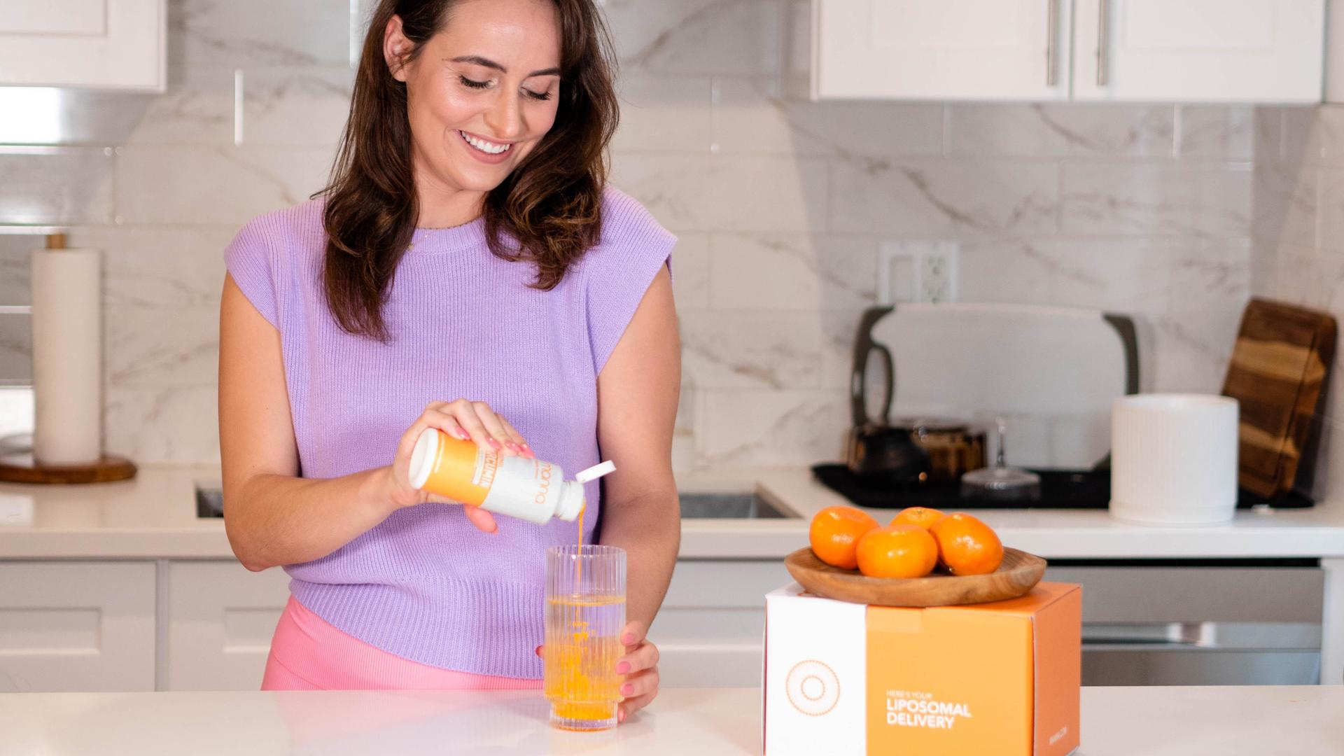 Woman pouring a bottle of Liposomal Curcumin into a glass of water on the kitchen counter.