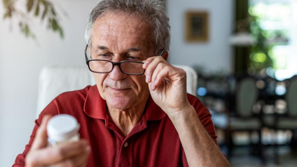 Older man using reading glasses to read the back off a pill bottle.