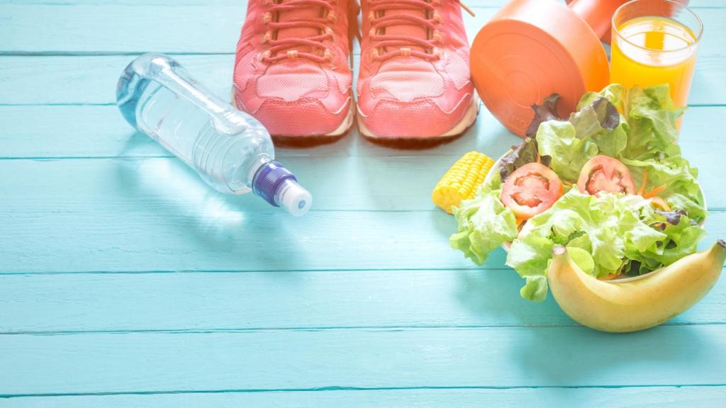 A water bottle, running shoes, a dumbbell, a banana, a salad, and a glass of juice on a light blue wooden surface.
