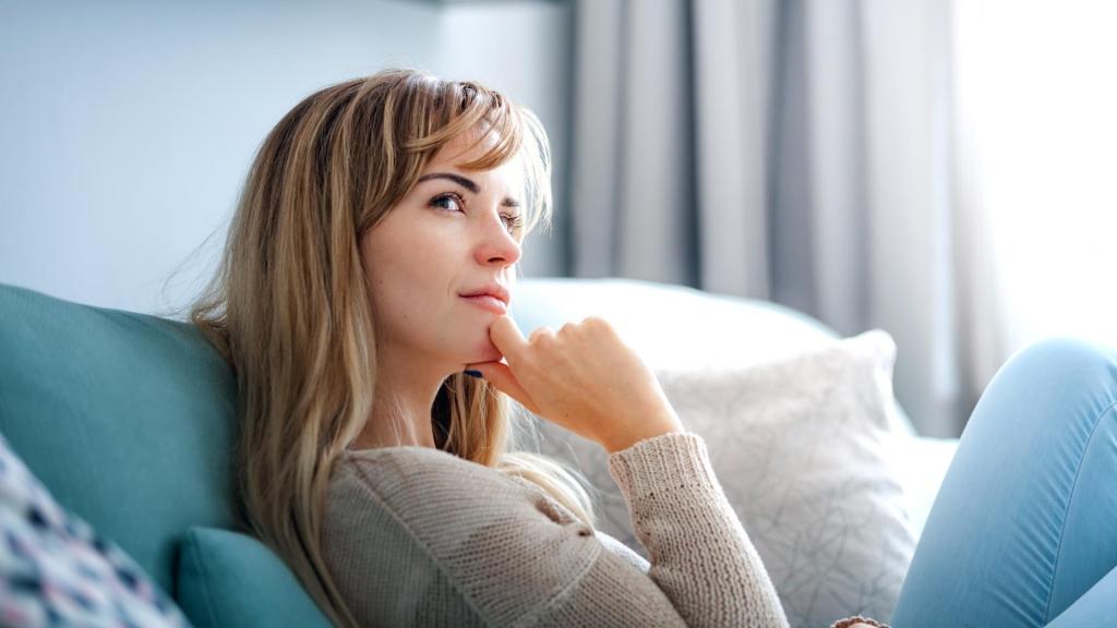 Woman looking off in the distance inquisitively while sitting on the couch.