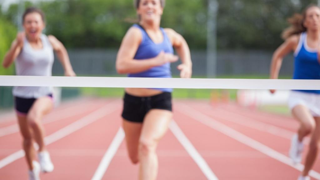 A finish line in the foreground with three women running towards it in the background.