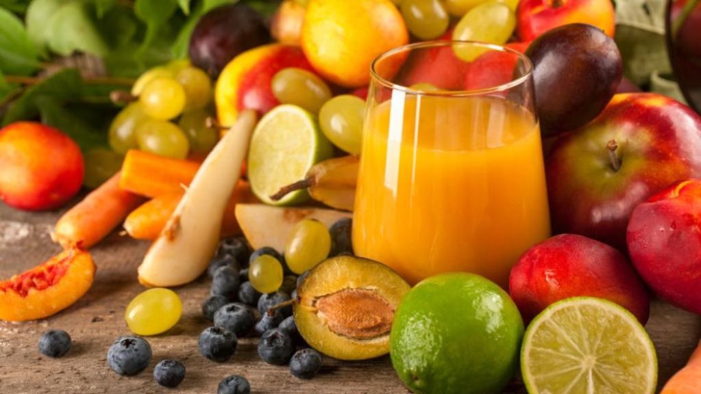 A variety of fresh fruits with a glass of orange juice on a wooden tabletop.