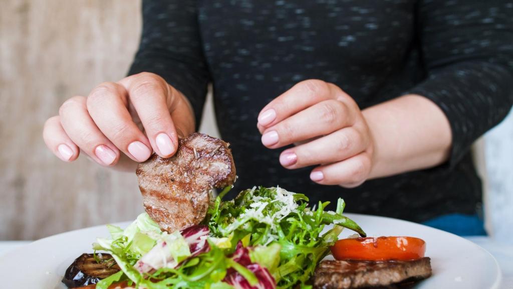 woman's hands placing a grilled steak on top of a salad.