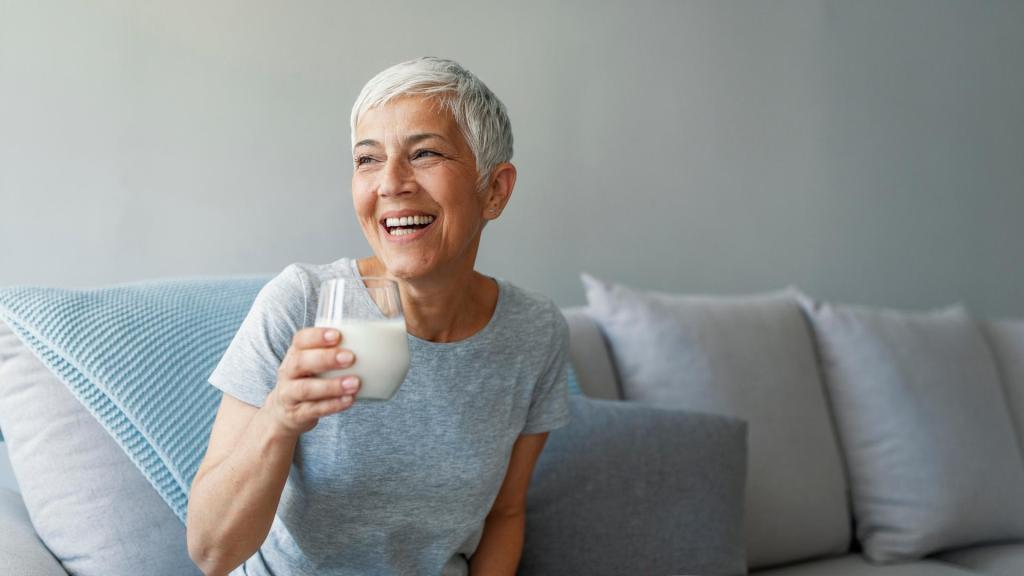 older woman drinking milk on the couch and smiling