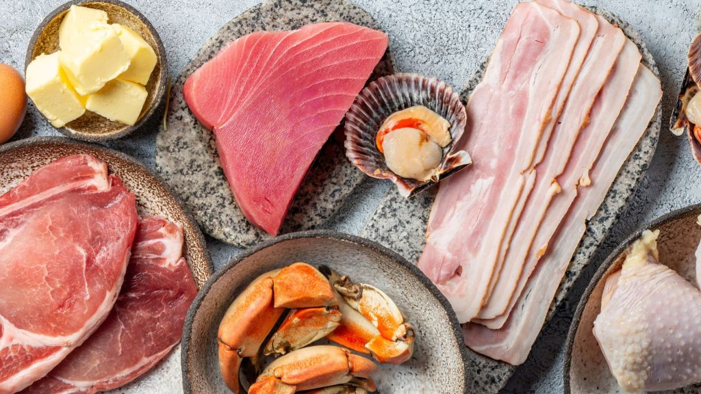 Assorted raw meats and seafood, including pork, beef, bacon, crab claws, tuna, scallop, and butter, are arranged on stone plates.