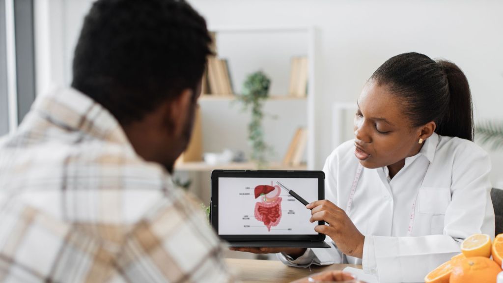 A doctor explains a digestive system diagram on a tablet to a patient.