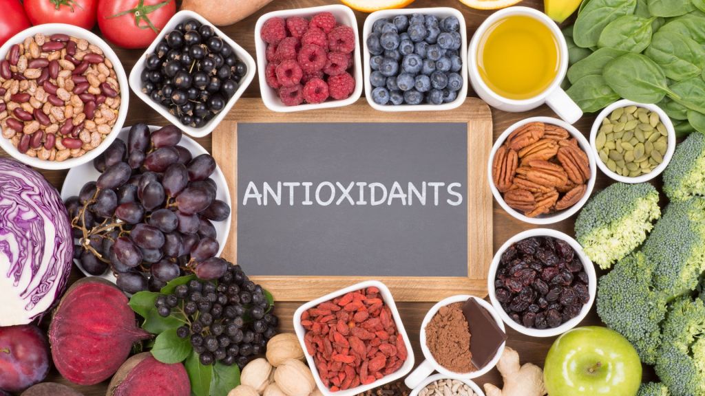 Various antioxidant-rich foods, including fruits, vegetables, seeds, nuts, and a small chalkboard with the word "ANTIOXIDANTS" in the center.