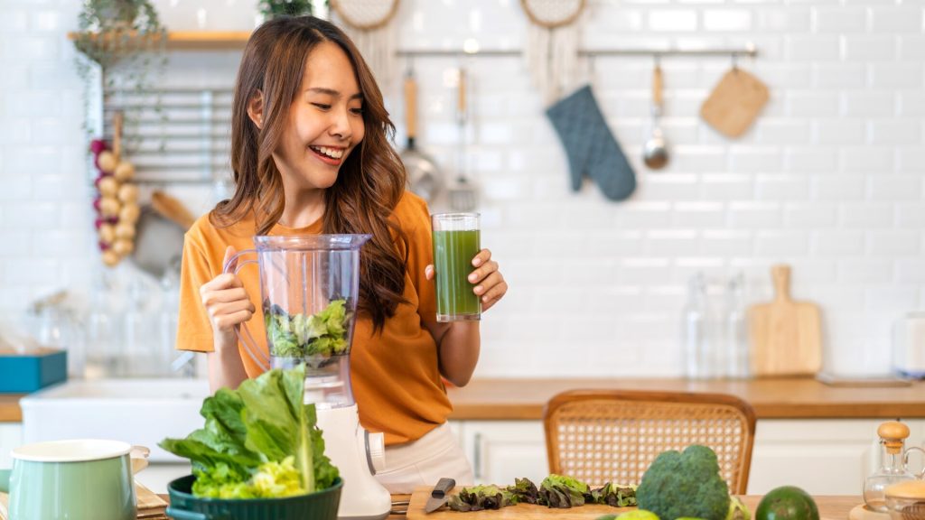 Woman blending greens into a smoothie and smiling.