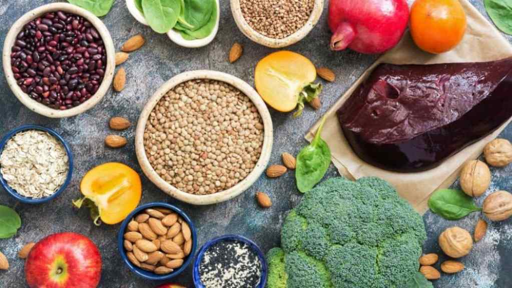 Assorted healthy foods including fruits, vegetables, nuts, and grains arranged on a textured surface.